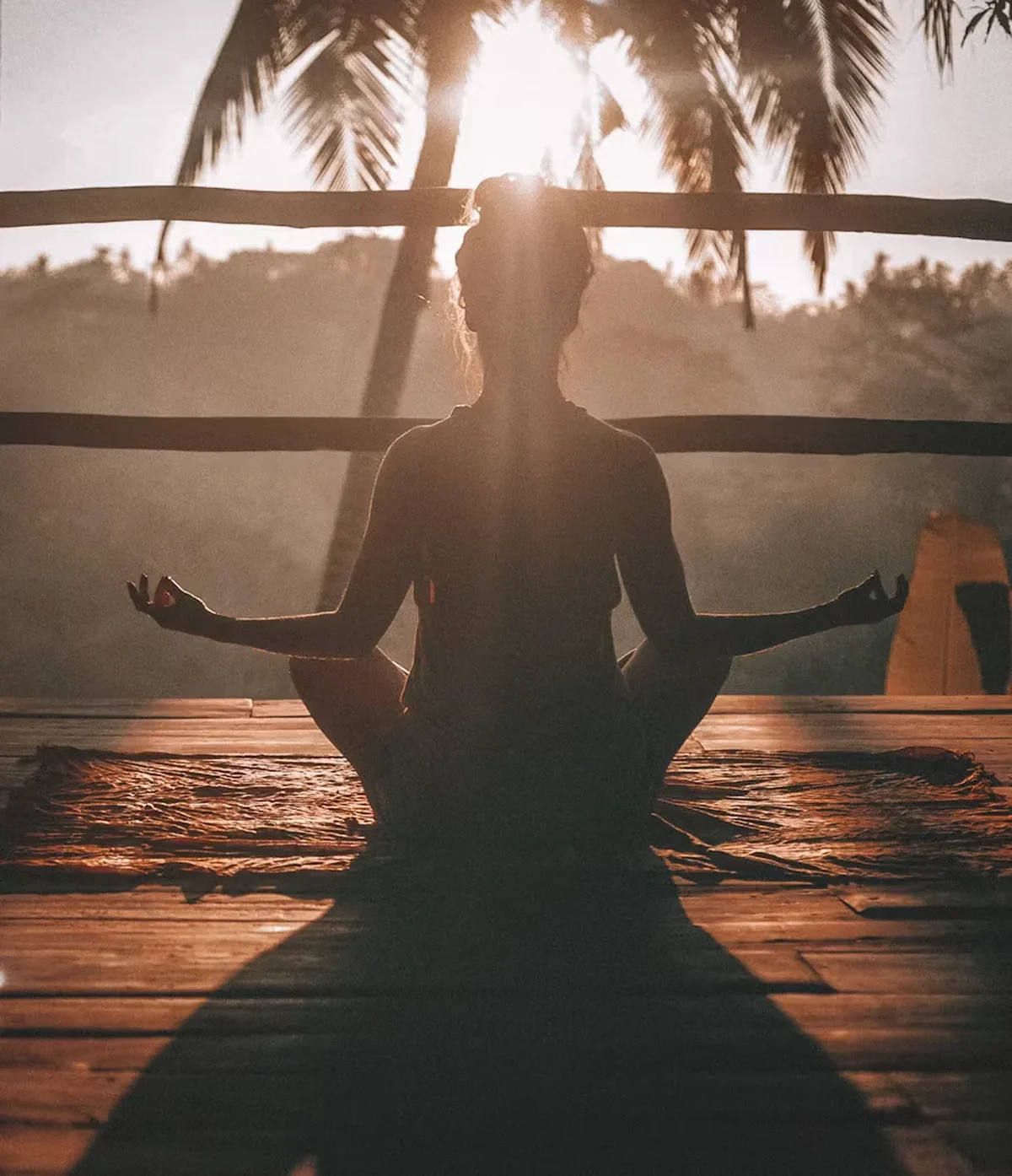 Woman meditating on a wooden deck at sunrise